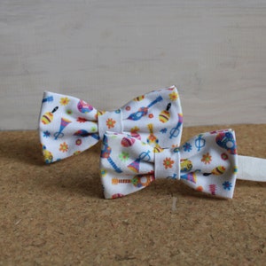 Può includere: Due papillon bianchi con un motivo colorato di strumenti musicali e fiori.