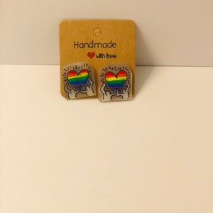 Pode incluir: Um par de brincos de coração arco-íris com fundo branco e o texto "Handmade with love".