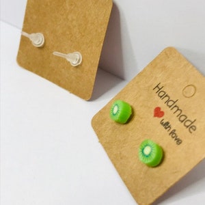 Peut inclure: Deux paires de boucles d'oreilles en forme de kiwi sur du carton brun avec le texte "Handmade with love".