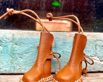 Puede incluir: Dos botas de cuero marrón con costuras blancas alrededor de los bordes. Las botas están atadas juntas con un cordón de cuero marrón.