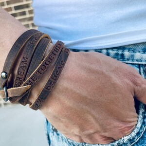 May include: A brown leather wrap bracelet with the words "Dream", "Be", "Me Together", and "Believe" engraved on it.