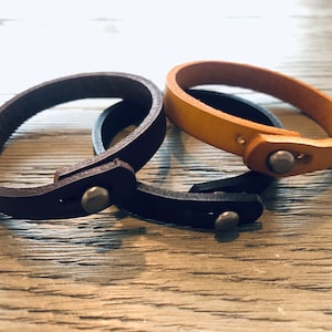 May include: Three leather bracelets with silver metal clasps. The bracelets are brown, tan, and black.