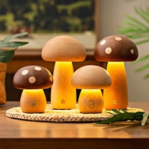 以下が含まれることがあります： 木製のキノコ型ランプ4個セット。2つは白い水玉模様の茶色の傘、他の2つは天然木の色合いの傘です。ランプは内側から照らされ、温かい光を放ちます。織り込まれたマットの上に配置されています。