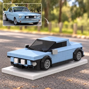 Op de afbeelding: Een lichtblauwe modelauto gebouwd van bouwstenen met een zwarte voorruit, zwarte wielkasten en zilverkleurige wielen. Het model staat op een rechthoekige witte basis. Een kleine afbeelding toont een lichtblauwe vintage auto ter vergelijking.