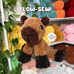 May include: A handmade, plush capybara toy in shades of brown and black. The capybara has a textured, fuzzy appearance, with a dark brown face and legs, and a lighter brown body. The text "LOW-SEW!" and "PDF PATTERN ONLY" are visible.