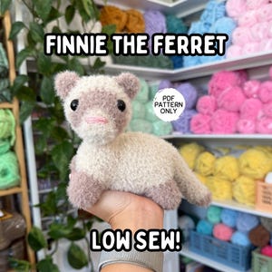 Könnte beinhalten: Ein handgefertigtes Frettchen-Plüschtier, hauptsächlich cremefarben mit hellvioletten Akzenten an Ohren, Pfoten und Schwanz. Das Spielzeug hat schwarze Augen und einen rosa Mund. Der Text auf dem Bild lautet "FINNIE THE FERRET" und "LOW SEW!"
