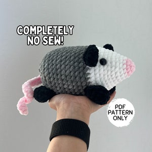 Könnte beinhalten: Ein gehäkeltes Plüsch-Opossum-Spielzeug in einem Grau-, Weiß- und Schwarz-Farbschema. Das Spielzeug wird in einer Hand mit einem schwarzen Armband gehalten. Der Text "COMPLETELY NO SEW!" ist über dem Spielzeug sichtbar. Der Text "PDF PATTERN ONLY" ist unter dem Spielzeug sichtbar.