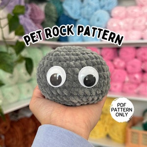 May include: A crocheted gray rock with large googly eyes. The text "PET ROCK PATTERN" is displayed above the rock. The words "PDF PATTERN ONLY" are in a circle below the rock.