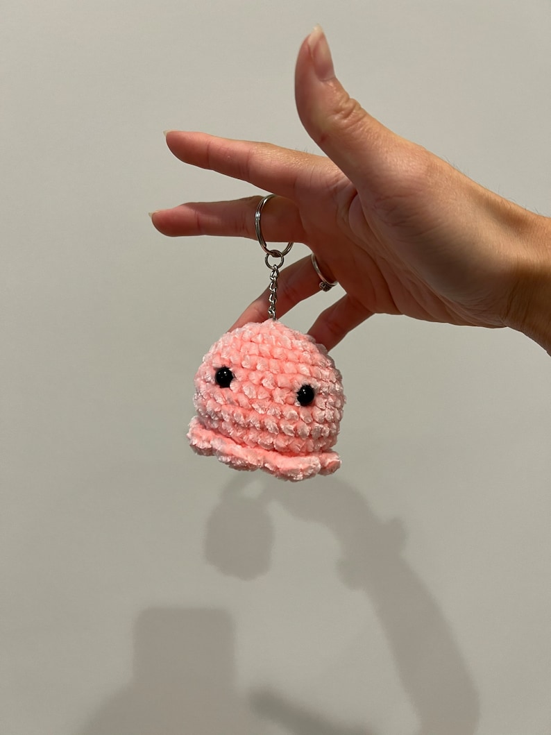 Op de afbeelding: Een roze gehaakte octopus sleutelhanger met zwarte ogen.