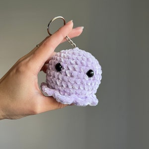 Op de afbeelding: Een paarse gehaakte octopus sleutelhanger met zwarte ogen.