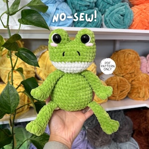 Op de afbeelding: Een groene gehaakte kikker met zwarte ogen, roze wangen en een witte mond. De tekst "NO-SEW!" staat boven de kikker en "PDF PATTERN ONLY" staat rechts. Het is een pluche speelgoed.