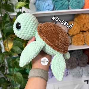 May include: A plush crochet turtle toy made with soft mint green yarn for the head and limbs, and a textured brown yarn for the shell. The turtle features large black plastic eyes and the text NO-SEW! and PDF PATTERN ONLY.