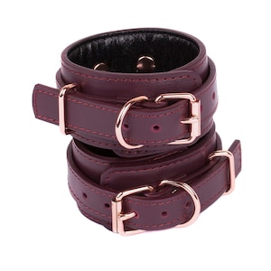 Pode incluir: Pulseiras de couro bordô com fivelas de ouro rosa. As pulseiras estão empilhadas umas sobre as outras.