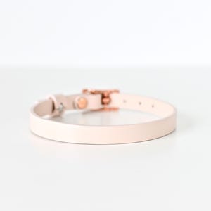 May include: A pale pink leather collar with a rose gold buckle and hardware. The collar is thin and appears to be for a small pet. The background is white.