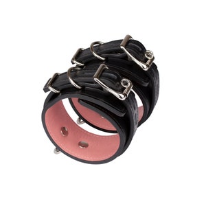 May include: Black leather restraints with silver buckles and a pink padded interior.