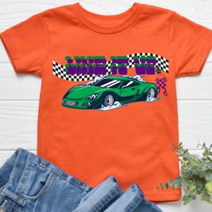 May include: Orange short-sleeved t-shirt with a green race car and the words "Live It Up" in purple and white. The car is driving on a checkered flag.