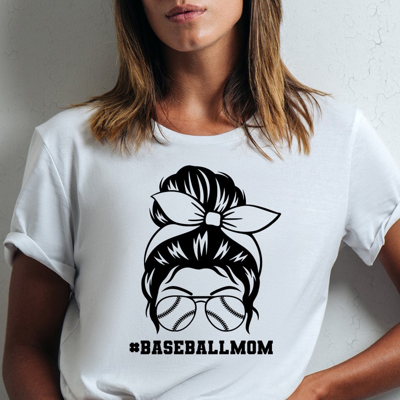 May include: White t-shirt with a black graphic of a woman with a messy bun, sunglasses with baseballs in the lenses, and a headband. The text #BASEBALLMOM is below the graphic.