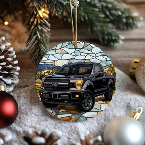 May include: A circular Christmas decoration depicting a black Ford pickup truck. The truck is set against a stained-glass style background with a landscape scene. The ornament has a gold hanging string.