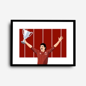 May include: A man in a red and white striped jersey holds up a silver trophy with both arms raised. He is smiling and has a moustache. The background is a red and white striped wall.