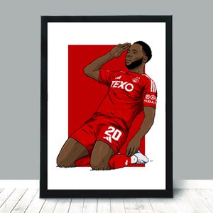 May include: Framed art print of a football player in a red kit, number 20, saluting. The player kneels against a red backdrop. The print is in a black frame.