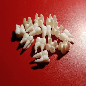 Puede incluir: Una colección de dientes de plástico blanco, dispuestos en un círculo sobre una superficie roja.