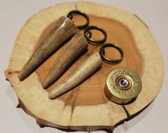 May include: Three antler keychains with brass key rings and a brass shotgun shell with the text "Fiocchi 20/70 Italy" on a wooden surface.