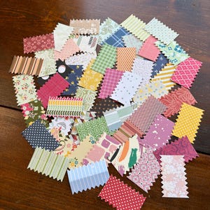 May include: A collection of small, colorful paper scraps with a zig-zag edge. The scraps feature various patterns, including stripes, polka dots, floral designs, and abstract shapes. The color palette includes red, pink, green, blue, and yellow.