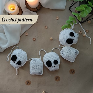 Puede incluir: Una guirnalda de crochet blanca con cuatro formas de calavera y dos lápidas. Las lápidas tienen la palabra "RIP" y un diseño de telaraña. La guirnalda es perfecta para la decoración de Halloween.