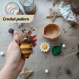May include: Crochet pattern for a cute bee amigurumi toy. The bee is brown and yellow with a friendly face. The pattern includes instructions for making a daisy and a leaf.