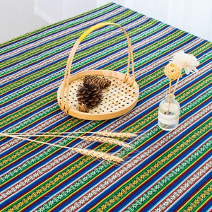 May include: A blue and green striped tablecloth with a woven basket and dried flowers in a glass vase. The tablecloth has a repeating pattern of small geometric shapes.