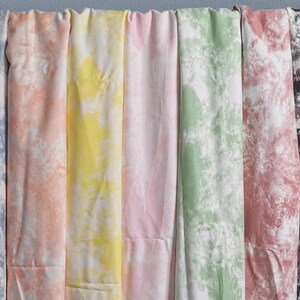 Pu&ograve; includere: Una collezione di otto campioni di tessuto in vari motivi tie-dye. I campioni sono disposti in fila da sinistra a destra, con i colori che vanno dal blu al rosa, dal giallo al verde, dal rosso al nero.
