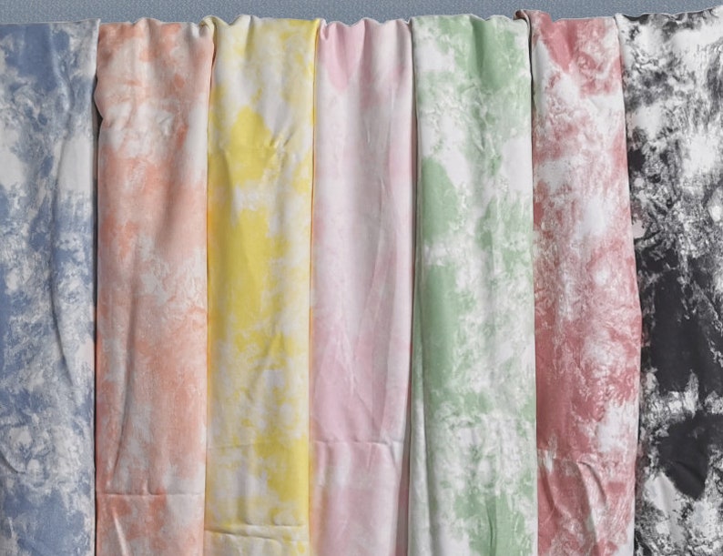Pu&ograve; includere: Una collezione di otto campioni di tessuto in vari motivi tie-dye. I campioni sono disposti in fila da sinistra a destra, con i colori che vanno dal blu al rosa, dal giallo al verde, dal rosso al nero.