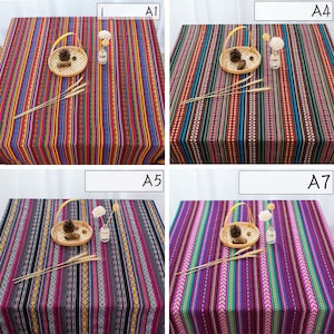May include: Four different striped tablecloths with various colors and patterns. The tablecloths are made of a woven fabric and have a fringed edge. The tablecloths are displayed on a table with a basket and a vase.