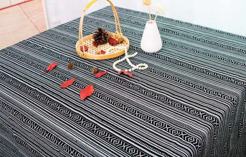 May include: Black and white striped tablecloth with a geometric pattern. The tablecloth is made of cotton and is perfect for a casual dining experience.