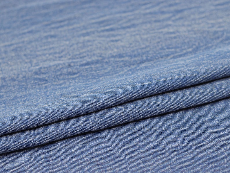 Puede incluir: Primer plano de una tela vaquera azul con una textura sutil. La tela est&aacute; doblada por la mitad, mostrando el tejido y el color azul claro.