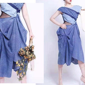 Puede incluir: Un vestido de mezclilla azul con un dise&ntilde;o en capas y un panel transparente en la cintura. El vestido tiene una silueta suelta y fluida y se estiliza con un par de sandalias de tac&oacute;n de pl&aacute;stico transparente.