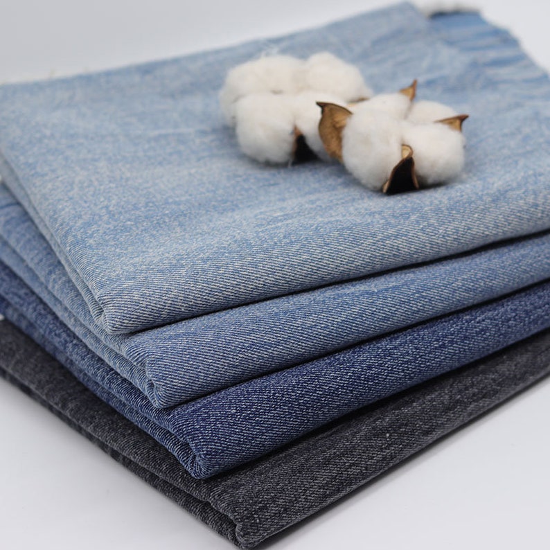 Puede incluir: Una pila de tela vaquera en varios tonos de azul y gris. La tela est&aacute; doblada cuidadosamente y tiene una superficie suave y texturizada.
