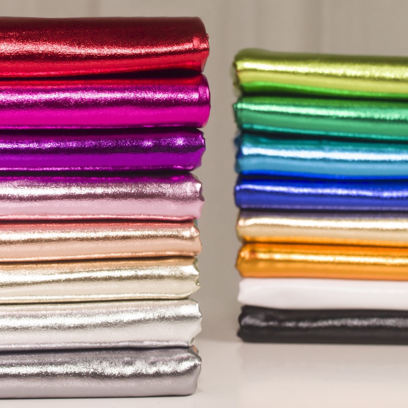 May include: A stack of metallic fabric in various colors, including red, pink, purple, gold, silver, and gray. The fabric is folded neatly and arranged in a vertical stack.