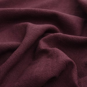 May include: Close-up of a deep burgundy fabric with a textured, linen-like weave. The fabric is folded and draped, showcasing its soft, drapey texture.