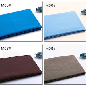 May include: Four fabric swatches in different colours: a bright blue, a light blue, a dark brown, and a light brown. The swatches are folded and laid out on a white surface. The swatches are labelled with the numbers M05, M06, M07, and M08.