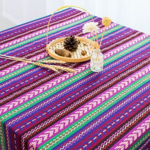 May include: A purple, green, and blue striped tablecloth with a woven pattern. The tablecloth is decorated with a wooden tray and a glass vase.