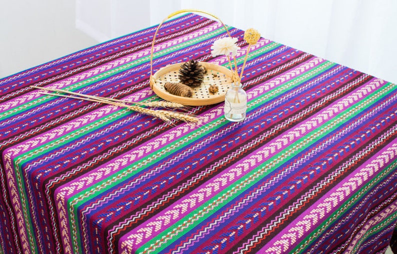 May include: A purple, green, and blue striped tablecloth with a woven pattern. The tablecloth is decorated with a wooden tray and a glass vase.