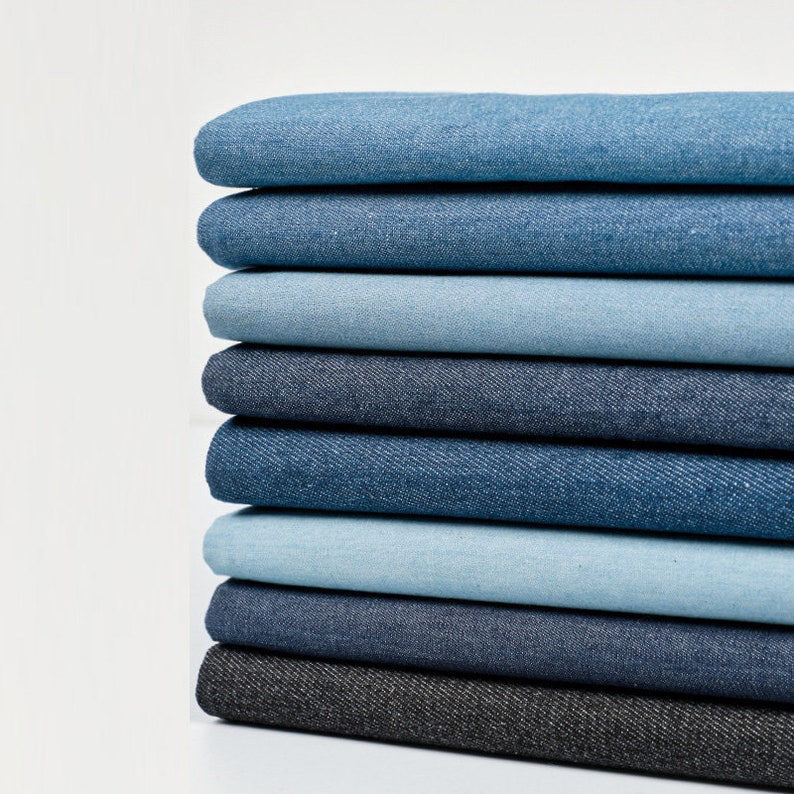 May include: A stack of eight different shades of denim fabric, ranging from dark blue to light blue.