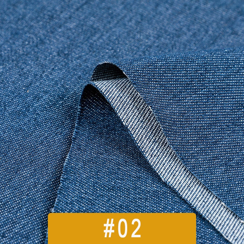 May include: Close-up of a blue denim fabric with a white weft. The fabric is folded over, showing the inside of the fabric. The fabric is labeled #02.
