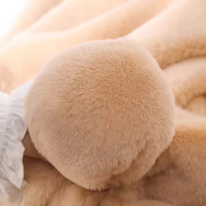 Peut inclure: Gros plan sur un tissu en fausse fourrure doux et brun clair. La fourrure est tr&egrave;s moelleuse et duveteuse, avec une texture lisse et uniforme.