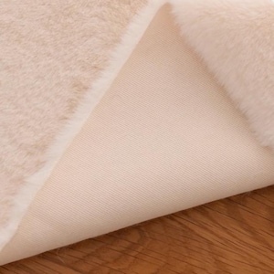 Peut inclure: Gros plan sur un tissu en fausse fourrure de couleur cr&egrave;me avec un envers blanc. Le tissu est doux et moelleux, et l'envers est lisse et uniforme.