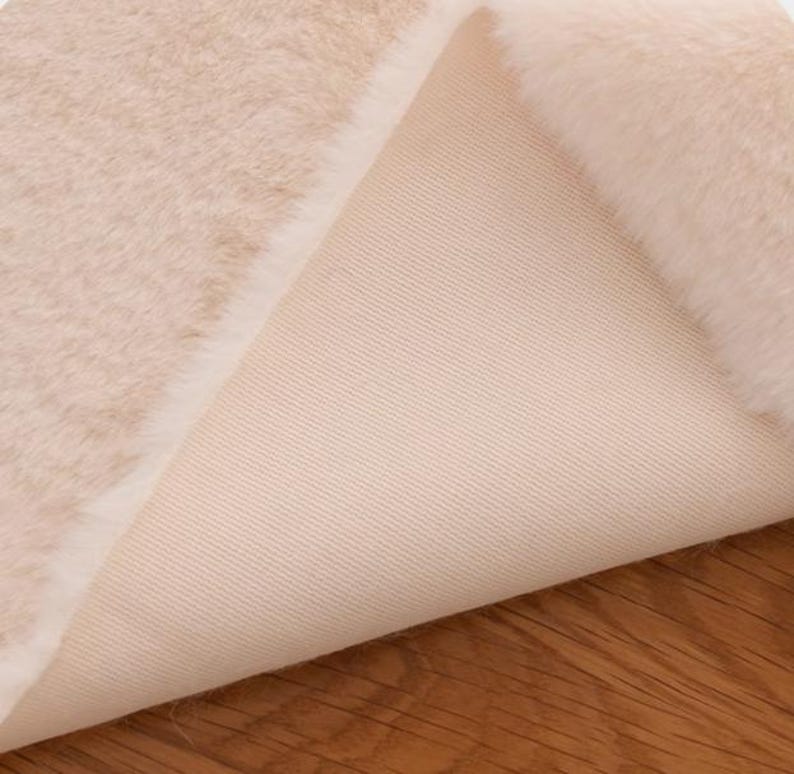 Peut inclure: Gros plan sur un tissu en fausse fourrure de couleur cr&egrave;me avec un envers blanc. Le tissu est doux et moelleux, et l'envers est lisse et uniforme.