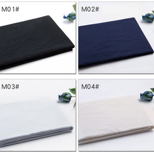May include: Four fabric swatches in different colours: black, navy blue, white, and off-white. Each swatch is folded in half and laid flat on a white surface. The swatches are labelled with the numbers M01, M02, M03, and M04.