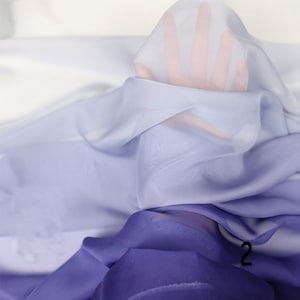 K&ouml;nnte beinhalten: Ein Farbverlaufsstoff in den Farben Hellblau, Lavendel und Lila. Der Stoff ist durchsichtig und hat eine weiche, flie&szlig;ende Textur.