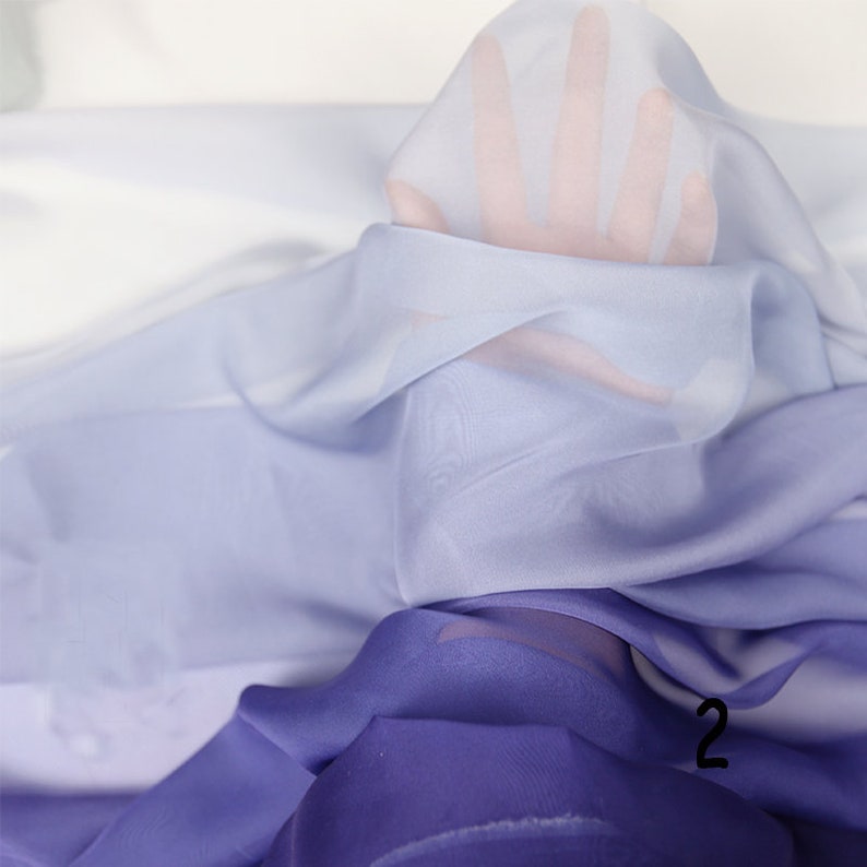 K&ouml;nnte beinhalten: Ein Farbverlaufsstoff in den Farben Hellblau, Lavendel und Lila. Der Stoff ist durchsichtig und hat eine weiche, flie&szlig;ende Textur.